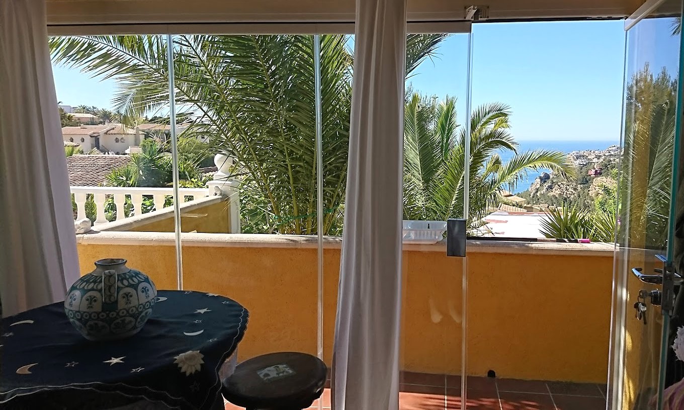 Terrasse fermée par des rideaux de verre, offrant un espace de détente avec vue sur la mer Méditerranée et le jardin méditerranéen.
