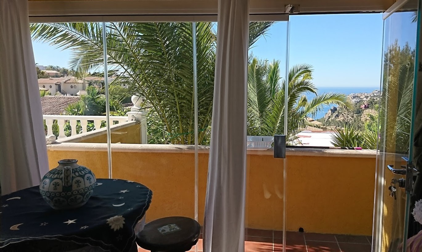 Terrasse vitrée avec rideaux de verre offrant une vue sur la mer Méditerranée et les palmiers, complétée par un sol en terre cuite.
