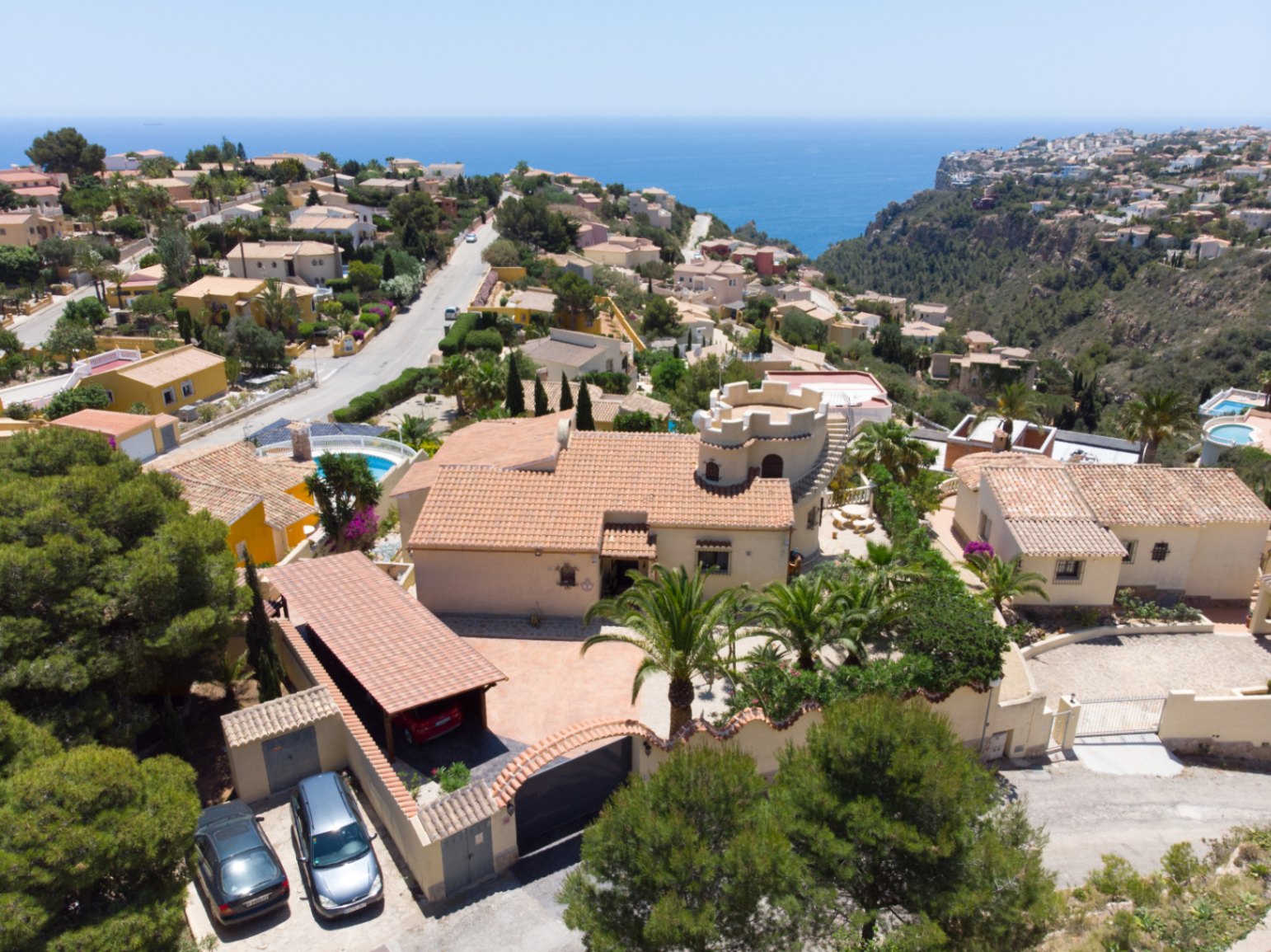 Vue aérienne de la villa soulignant sa tour distinctive, son abri pour voitures et son terrain paysager avec vue panoramique sur la mer Méditerranée.