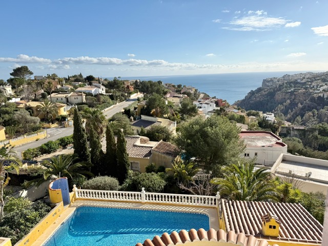 Vue surélevée sur la piscine privée avec balustrade blanche, offrant un panorama sur la mer Méditerranée et le quartier résidentiel verdoyant de Benitachell.