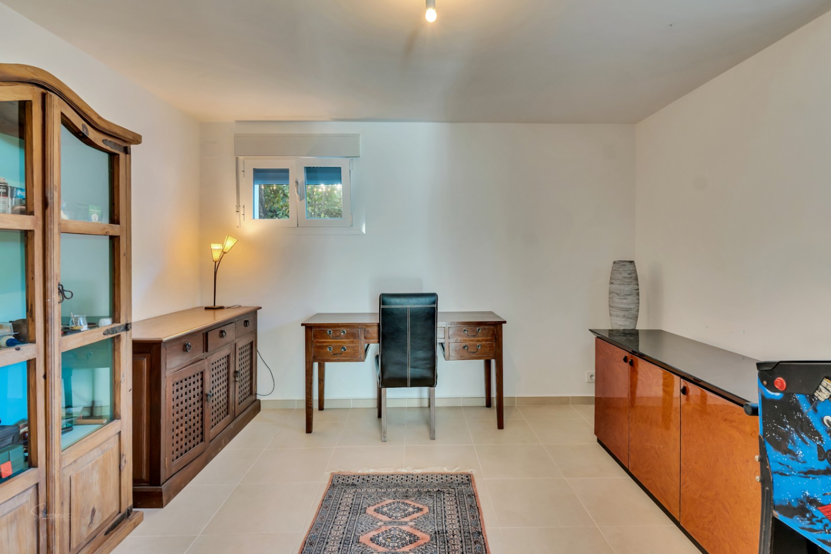 Bureau fonctionnel avec un bureau en bois classique, une chaise en cuir noir et des meubles rustiques. L'espace comprend une vitrine en bois et un sol en carrelage clair.