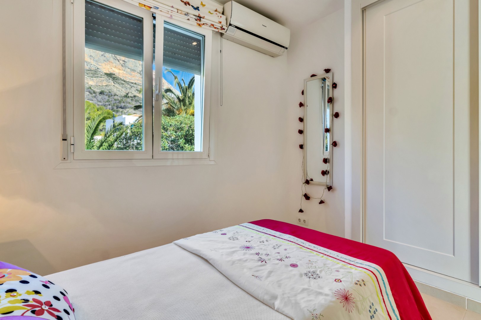 Chambre lumineuse avec climatisation, placard intégré et fenêtre offrant une vue dégagée sur le mont Montgó et les jardins environnants.
