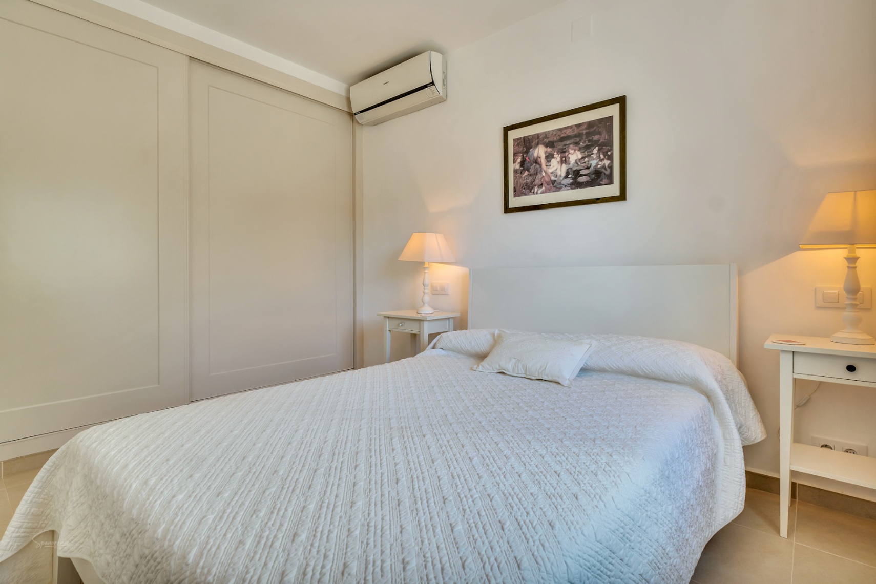 Chambre lumineuse avec de grands placards intégrés, climatisation individuelle et tables de chevet blanches sous un éclairage chaleureux et apaisant.