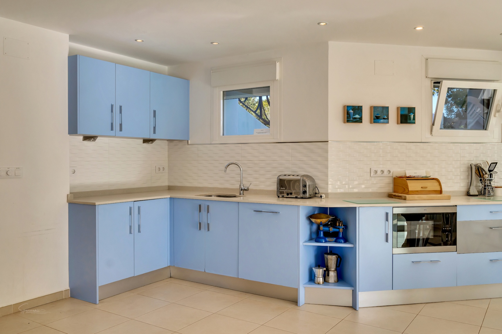 Cuisine moderne avec des meubles bleu pastel, un dosseret en carrelage blanc et un plan de travail clair. Équipée d'appareils intégrés et baignée de lumière naturelle.