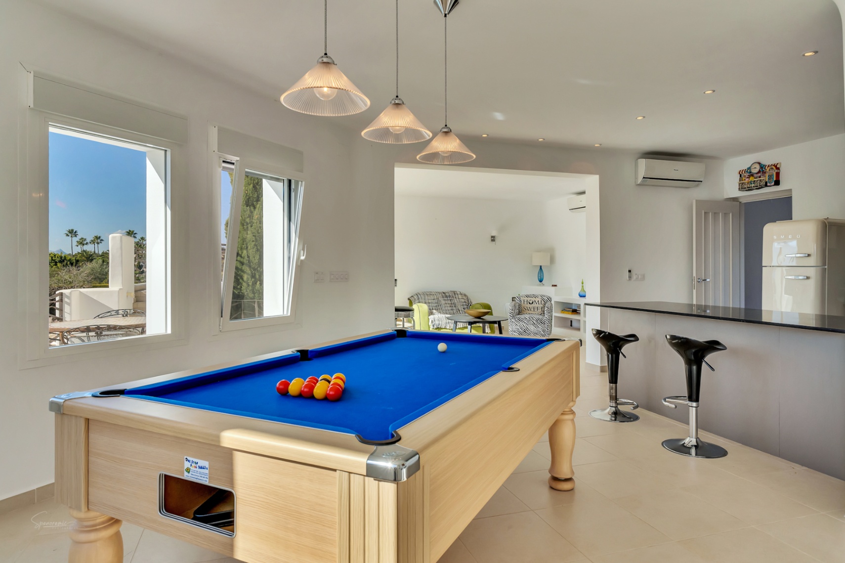Salle de divertissement avec billard, bar moderne et réfrigérateur au design rétro. Les grandes fenêtres illuminent l'espace et offrent une vue sur les extérieurs de la villa.