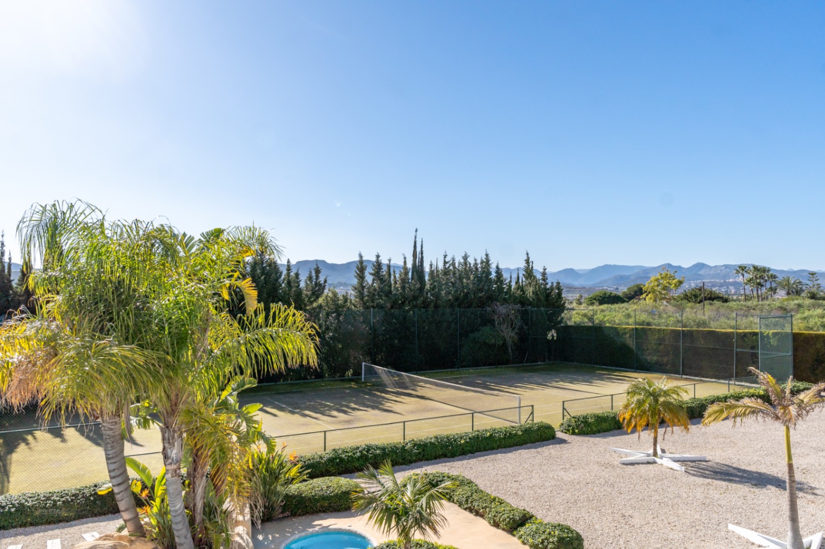 Vue surélevée du court de tennis privé entouré de haies et de palmiers, offrant une perspective sur la vallée et les montagnes environnantes.