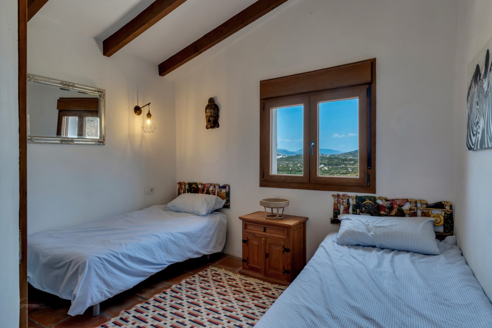 Chambre avec lits jumeaux, poutres apparentes et vue sur le paysage depuis la fenêtre à cadre en bois.