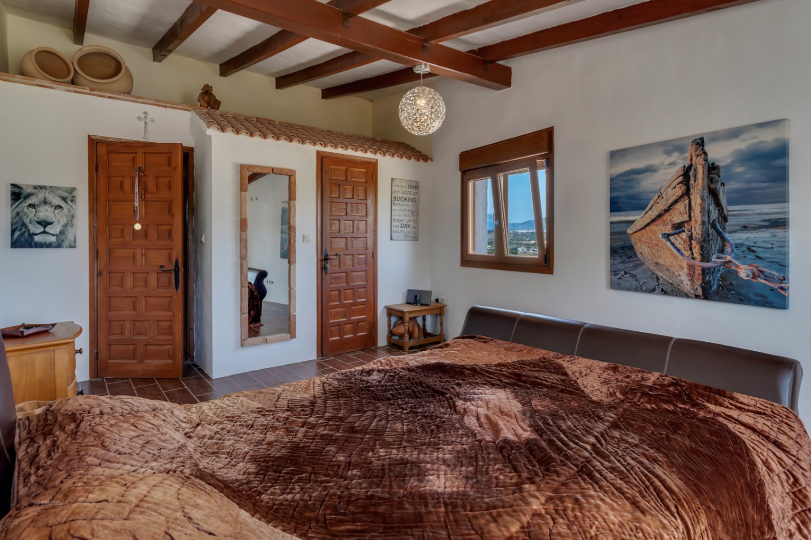 Chambre rustique avec poutres apparentes, carrelage et lit avec tête de lit en cuir marron.