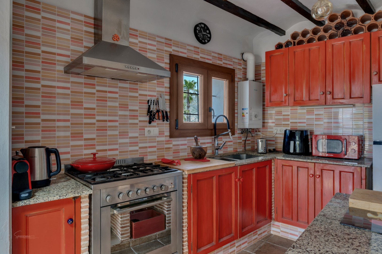 Cuisine rustique avec des carreaux colorés, des meubles en bois rougeâtre et des plans de travail en granit.