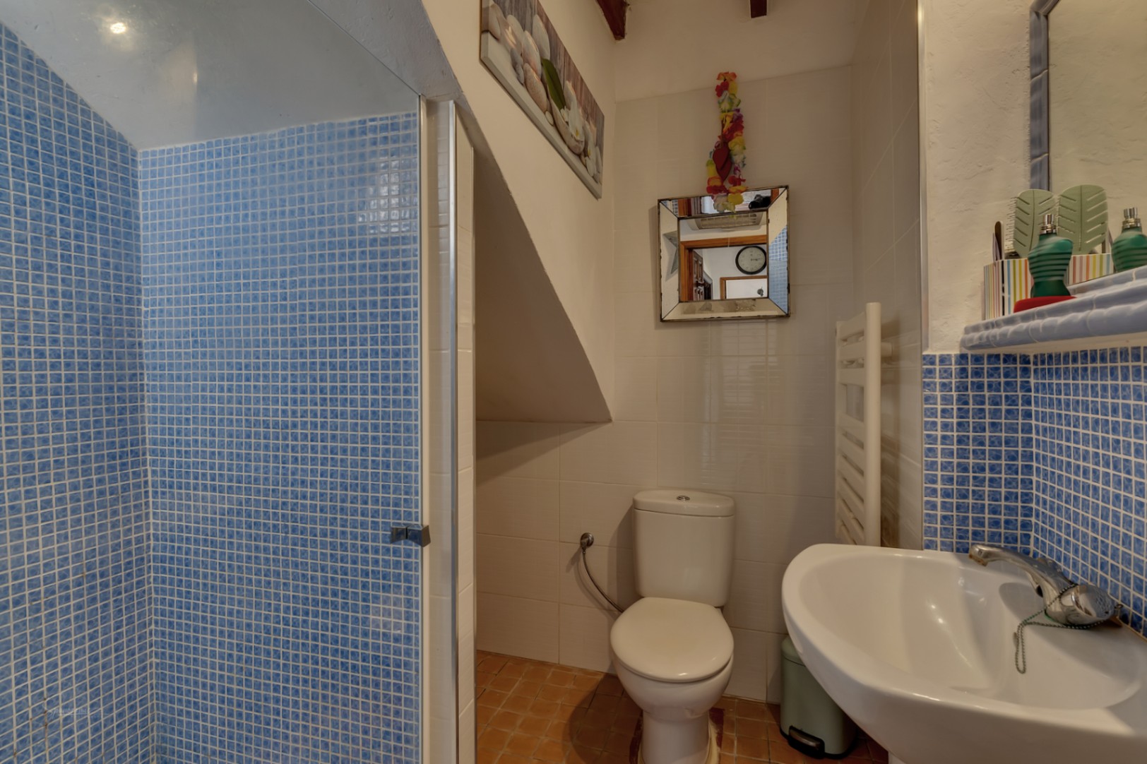 Détail de la salle de bain avec douche en mosaïque bleue, toilettes blanches et lavabo avec comptoir en mosaïque.