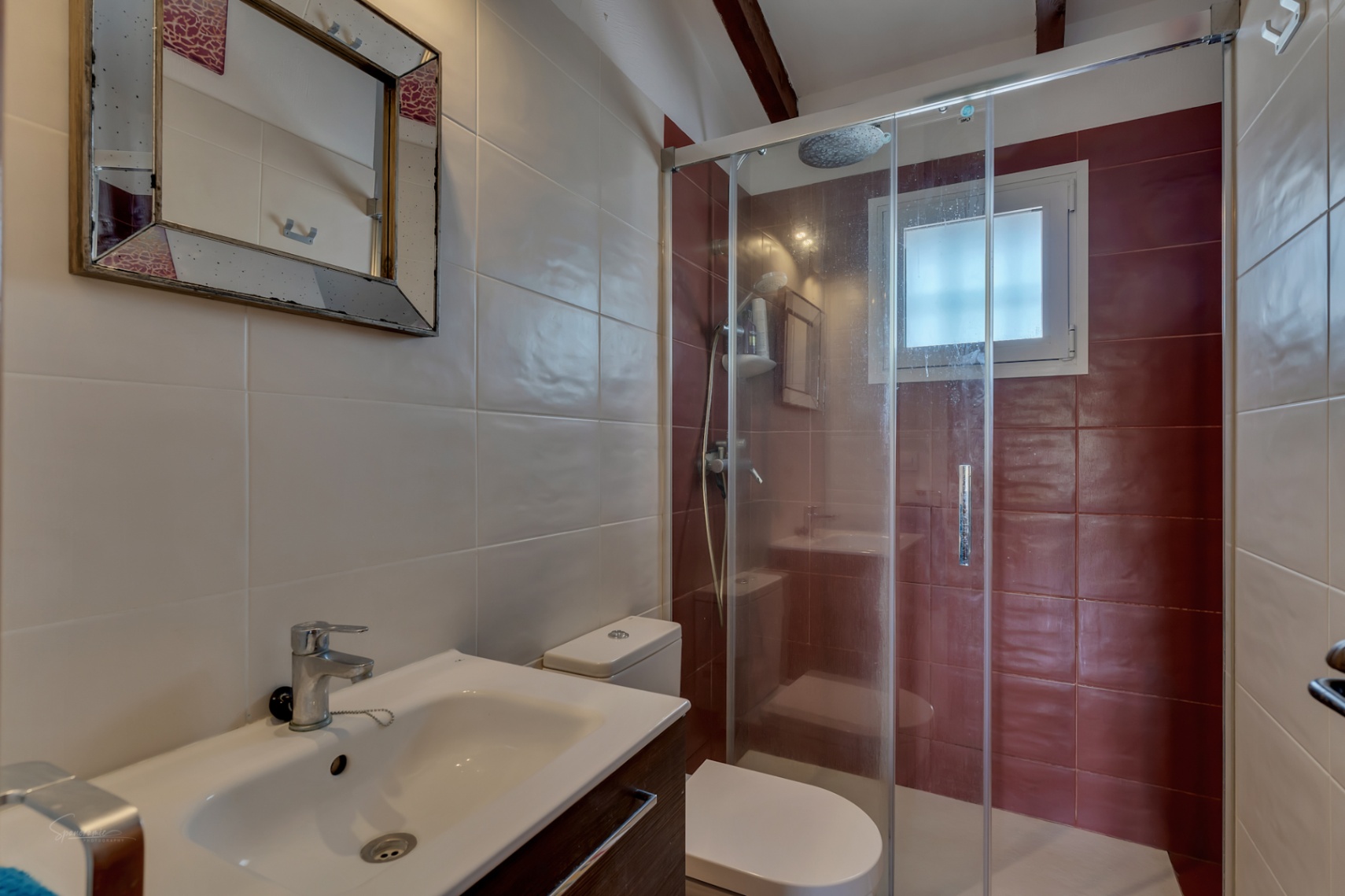 Détail de salle de bain avec douche en verre, lavabo moderne et carrelage dans les tons neutres et bordeaux.