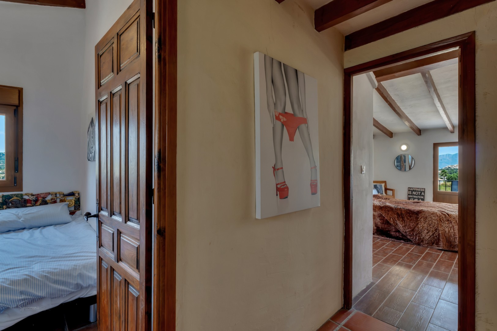 Détail du couloir avec portes en bois, carrelage rustique et œuvre d'art moderne au mur.