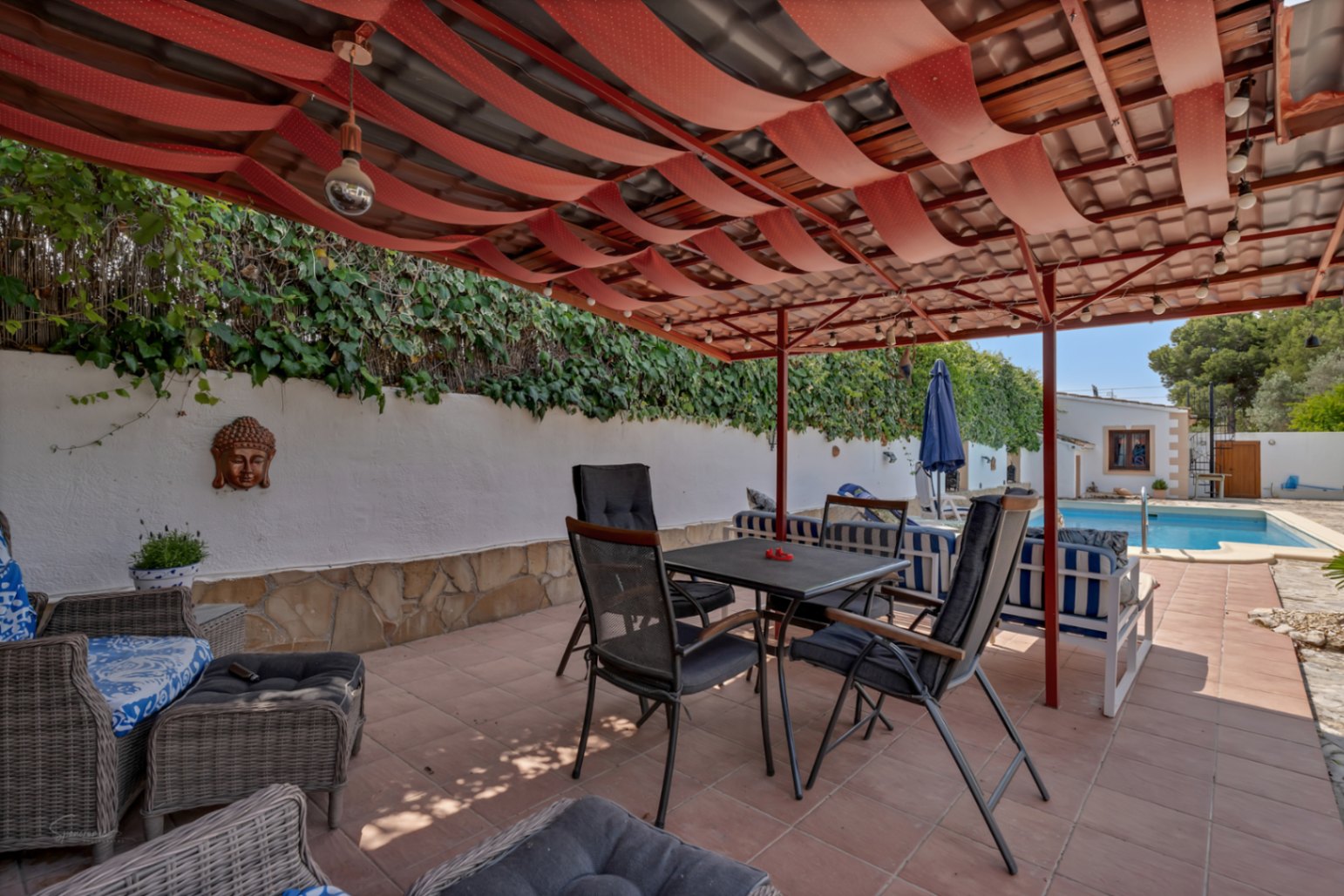 Terrasse couverte avec auvent rouge et sol carrelé. Mur blanc avec décor de Bouddha et jardin vertical.