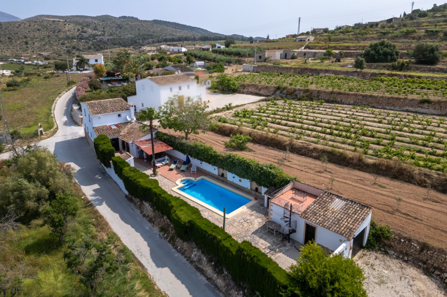 Vue aérienne d'une finca avec piscine bleue, jardin luxuriant et champs cultivés à Teulada, Costa Blanca.