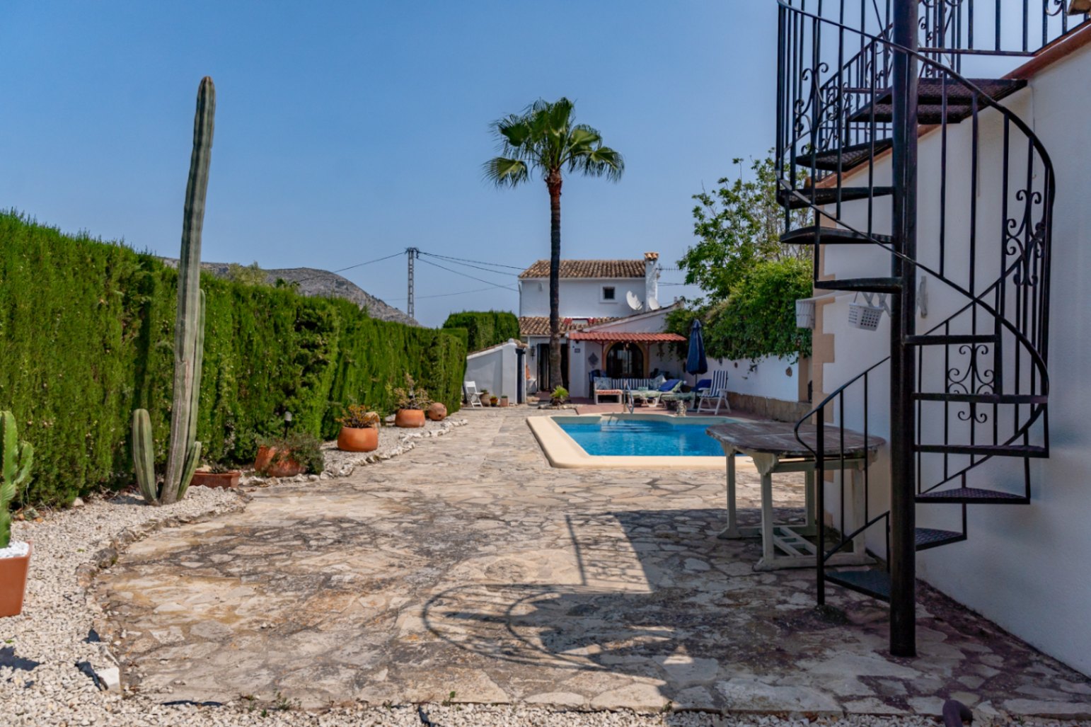 Vue sur le patio avec piscine, escalier en colimaçon en fer et haute haie à Teulada.