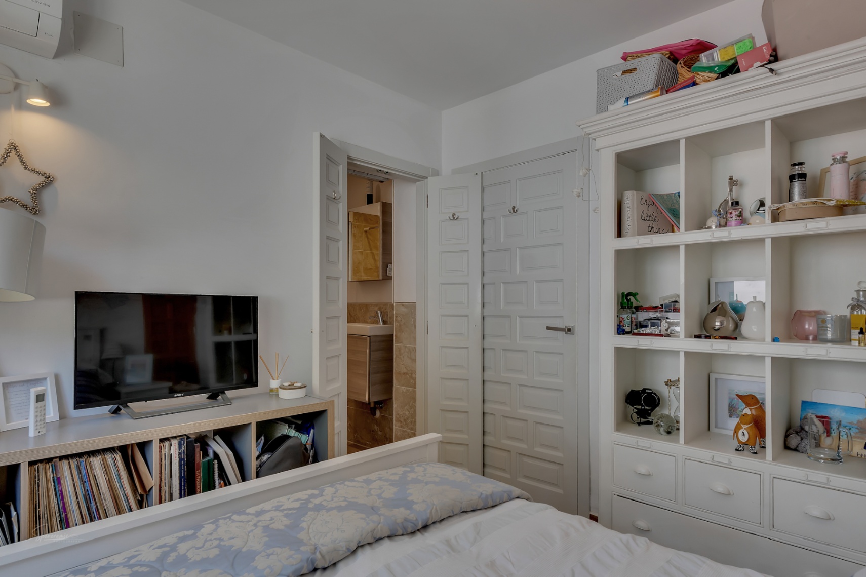 Chambre lumineuse avec étagères blanches et accès à la salle de bain attenante avec des accents de bois.