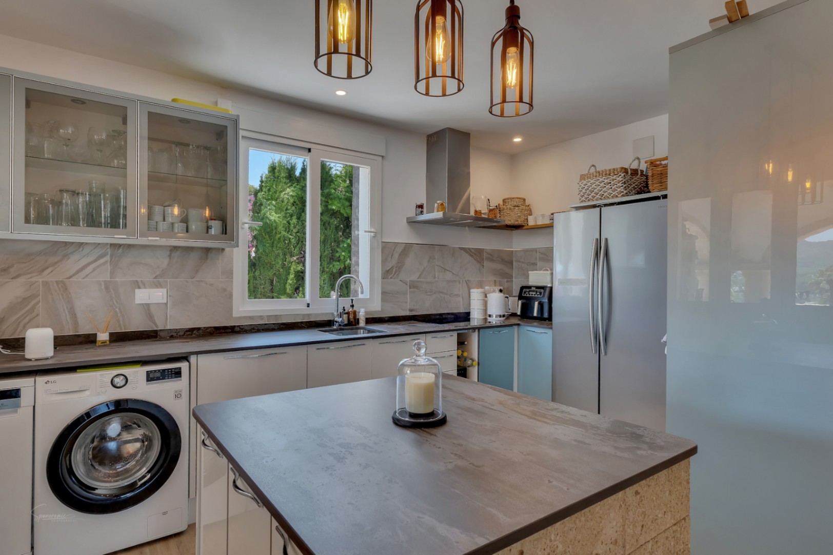 Cuisine moderne avec îlot central, électroménager intégré et luminaires suspendus design.