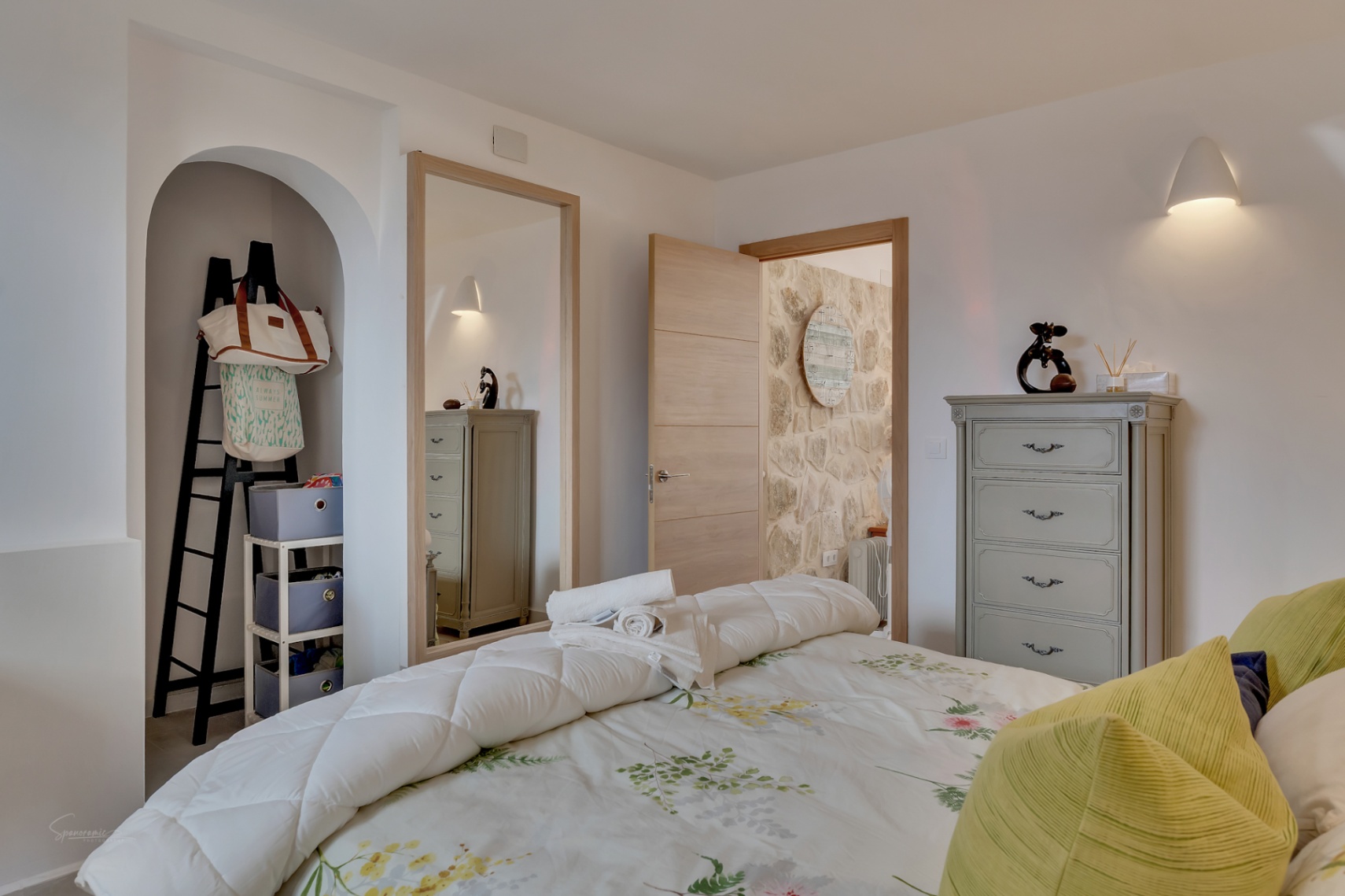 Détail de la chambre avec niche décorative, commode grise et literie florale.