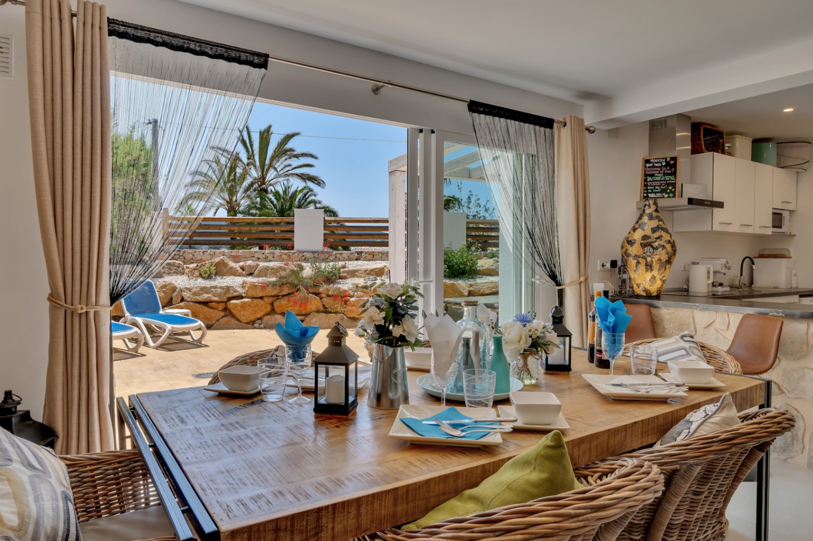 Salle à manger lumineuse avec table rustique et accès à une terrasse avec transats et jardin méditerranéen.