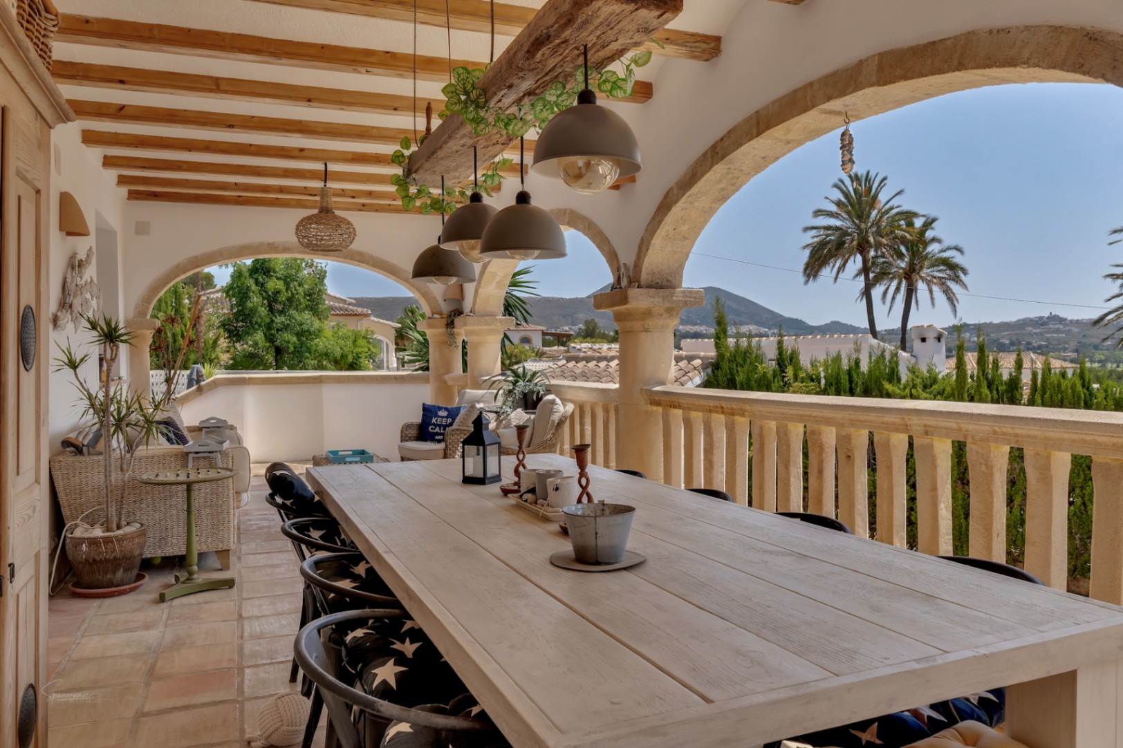 Terrasse couverte avec arches en pierre et table à manger en bois clair avec vue sur la montagne.