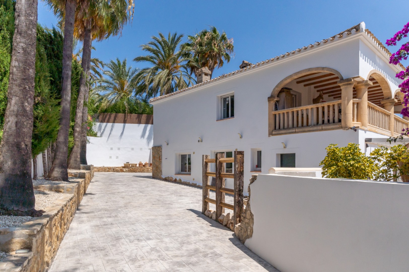 Vue extérieure de la villa à Jávea, avec allée en pierre et façade blanche. Balcon avec arches et colonnes.