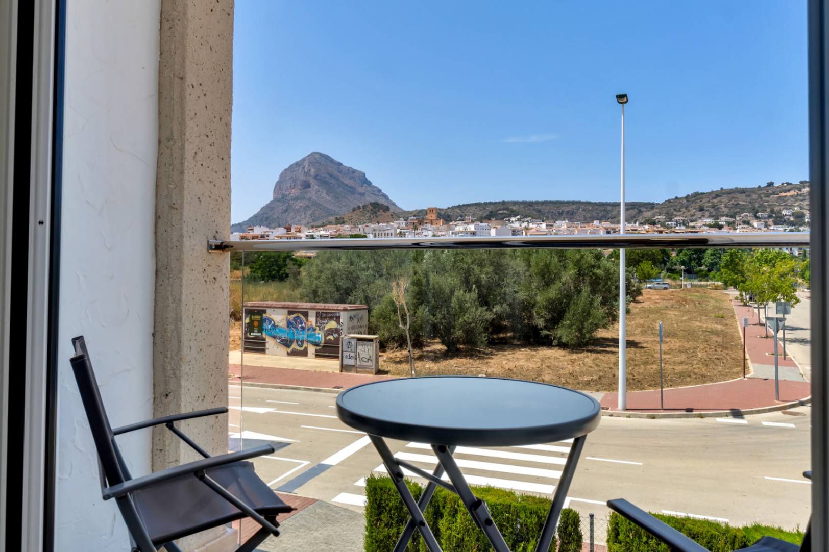 Balcon avec garde-corps en verre et mobilier noir, offrant une vue imprenable sur le mont Montgó et le vieux quartier de Jávea.