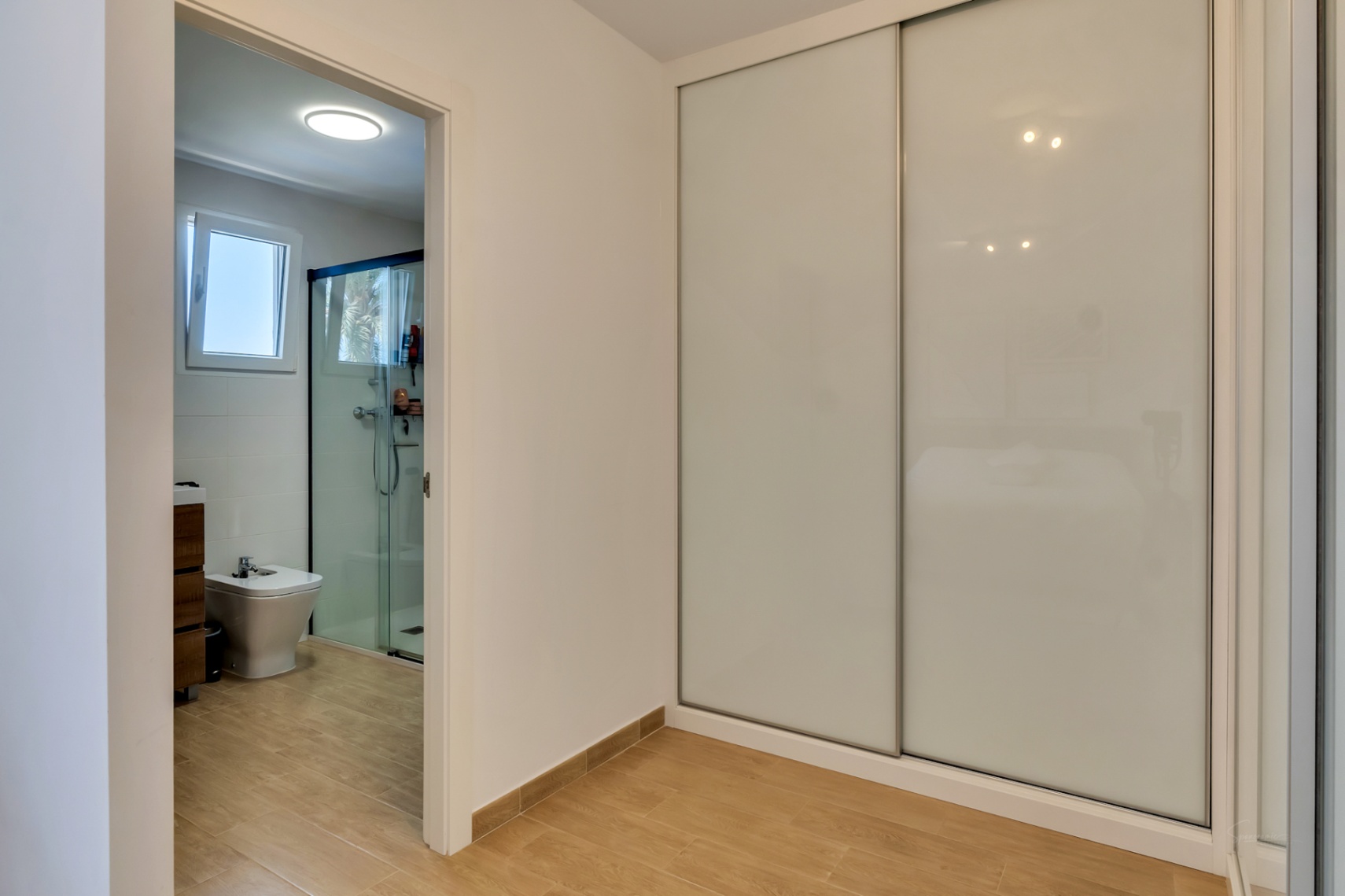 Chambre avec de grands placards intégrés aux portes coulissantes blanches et un accès direct à une salle de bain attenante avec douche à l'italienne.