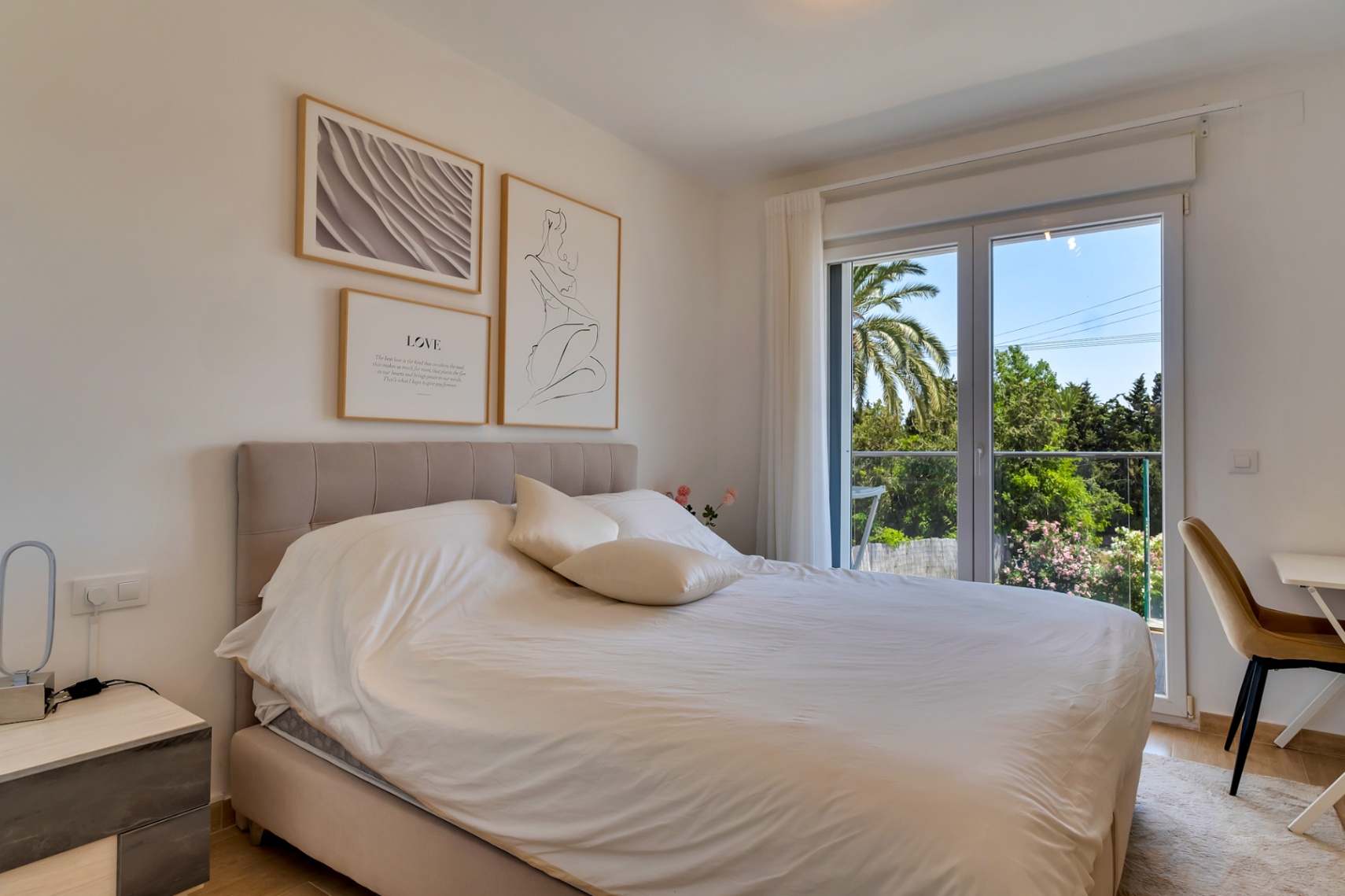 Chambre double avec tête de lit capitonnée, coin bureau et accès extérieur offrant une vue sur les jardins environnants.