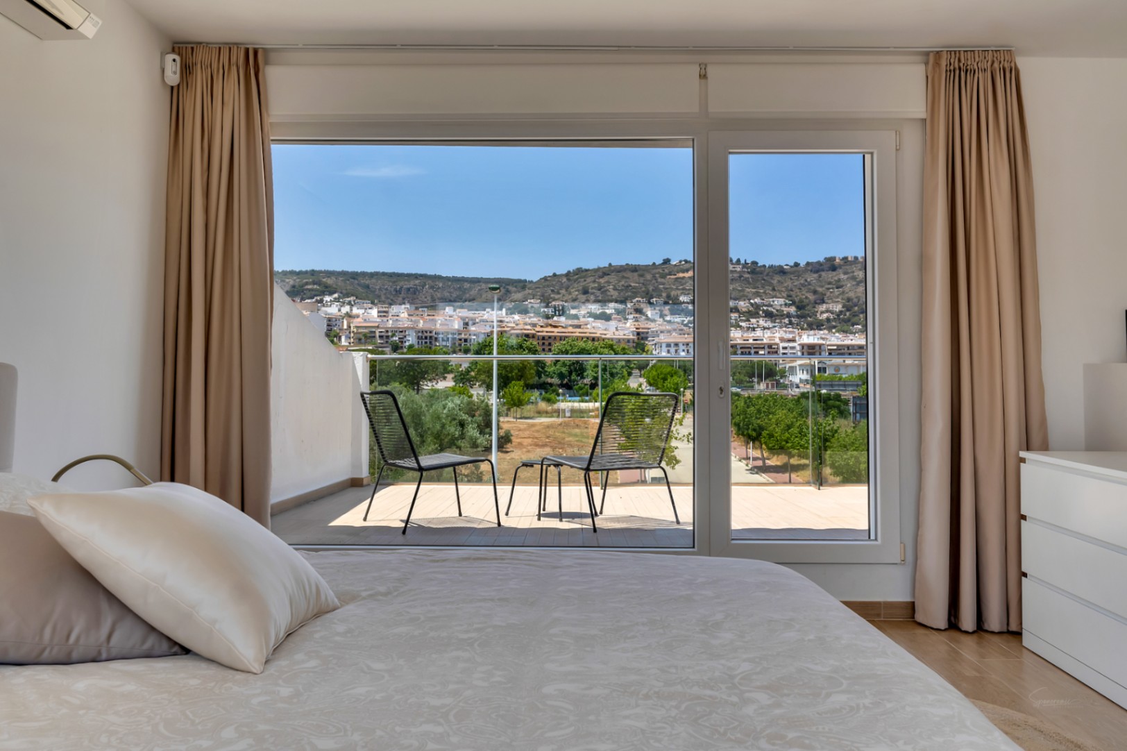 Chambre lumineuse avec accès direct à une terrasse privée meublée. Les grandes baies vitrées offrent une vue dégagée sur la ville et les collines environnantes.