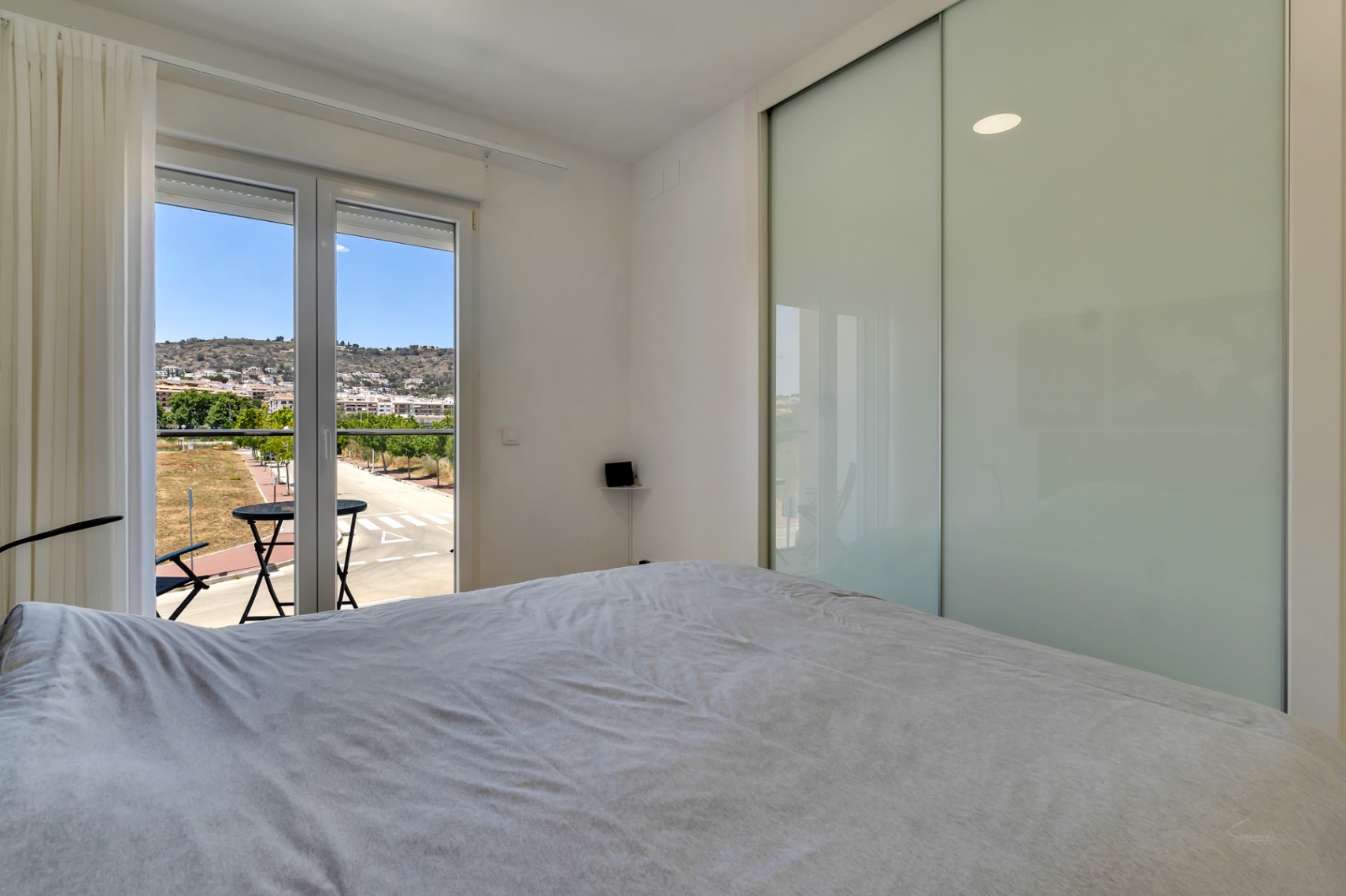Chambre lumineuse avec grand placard intégré à portes coulissantes et accès direct à un balcon privé offrant une vue dégagée sur les collines environnantes.