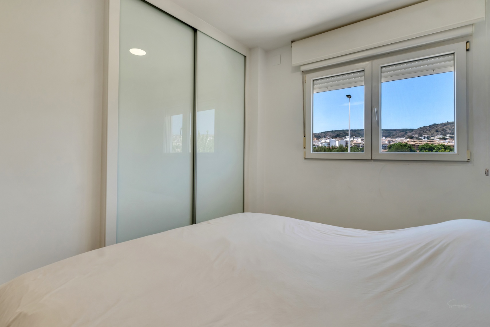 Chambre lumineuse avec placard intégré aux portes coulissantes en verre dépoli et fenêtre à double vitrage offrant une vue sur les collines environnantes.