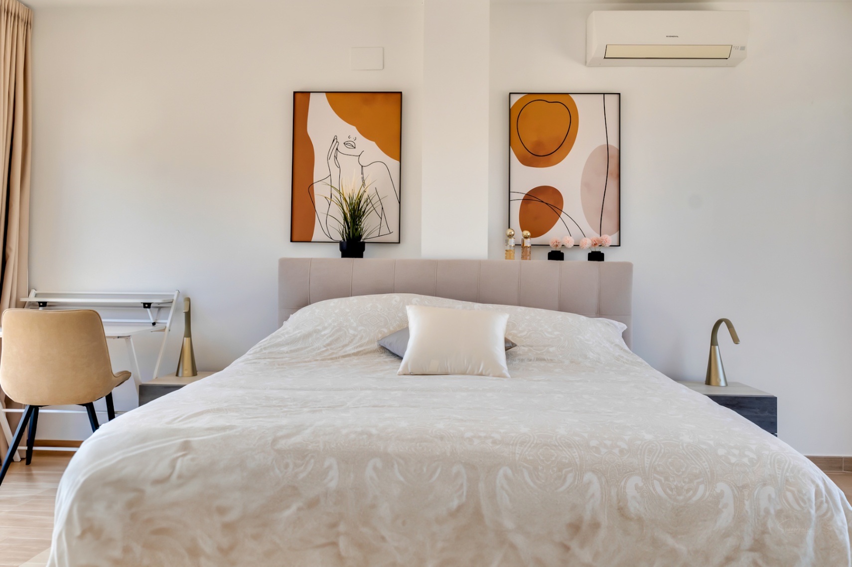 Chambre lumineuse avec tête de lit capitonnée, tableaux abstraits aux tons terreux et coin bureau. Équipée de la climatisation et de lampes au design minimaliste.