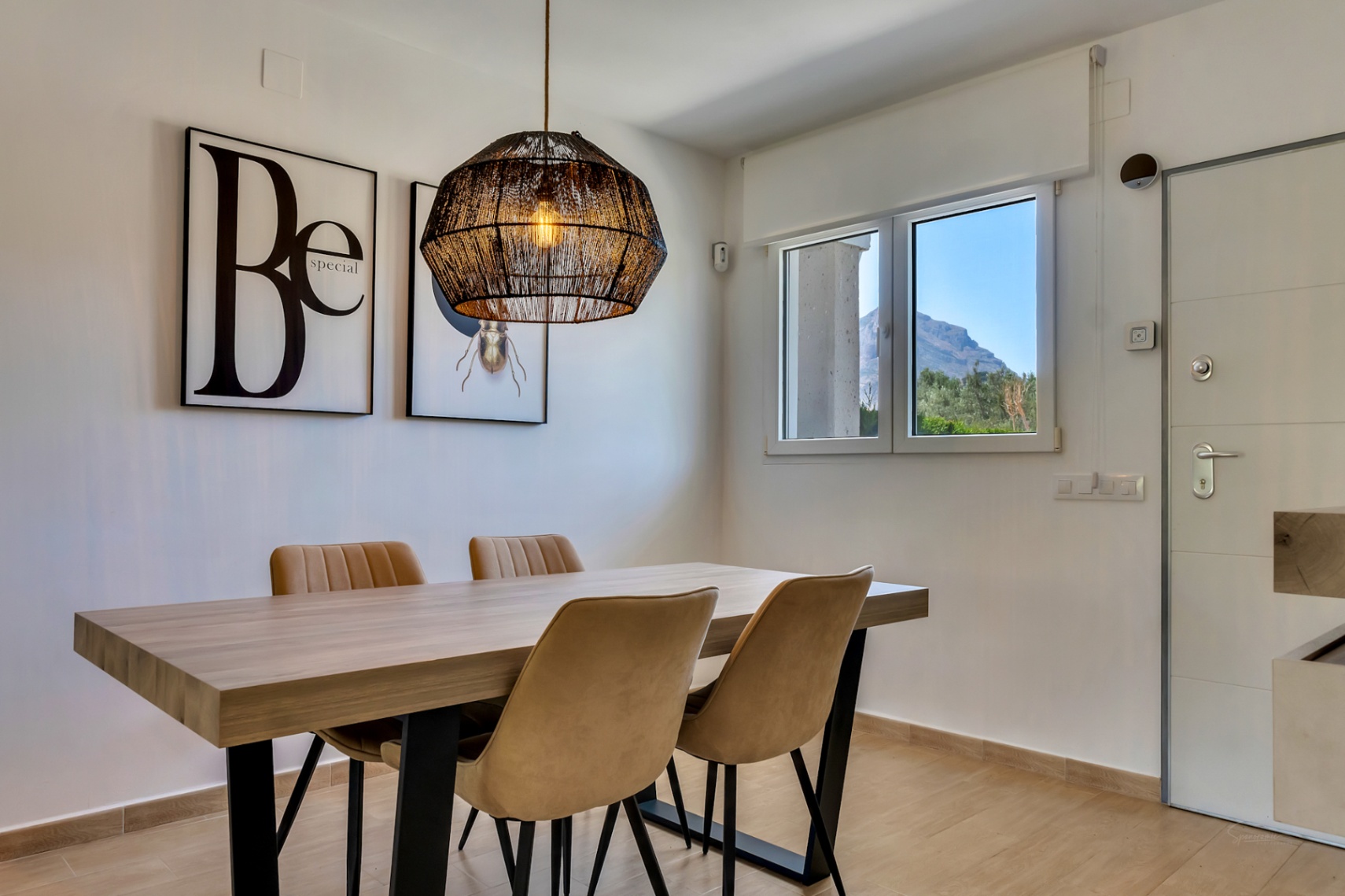 Espace salle à manger contemporain avec table en bois, suspension en fibres naturelles et vue sur le mont Montgó par la fenêtre.