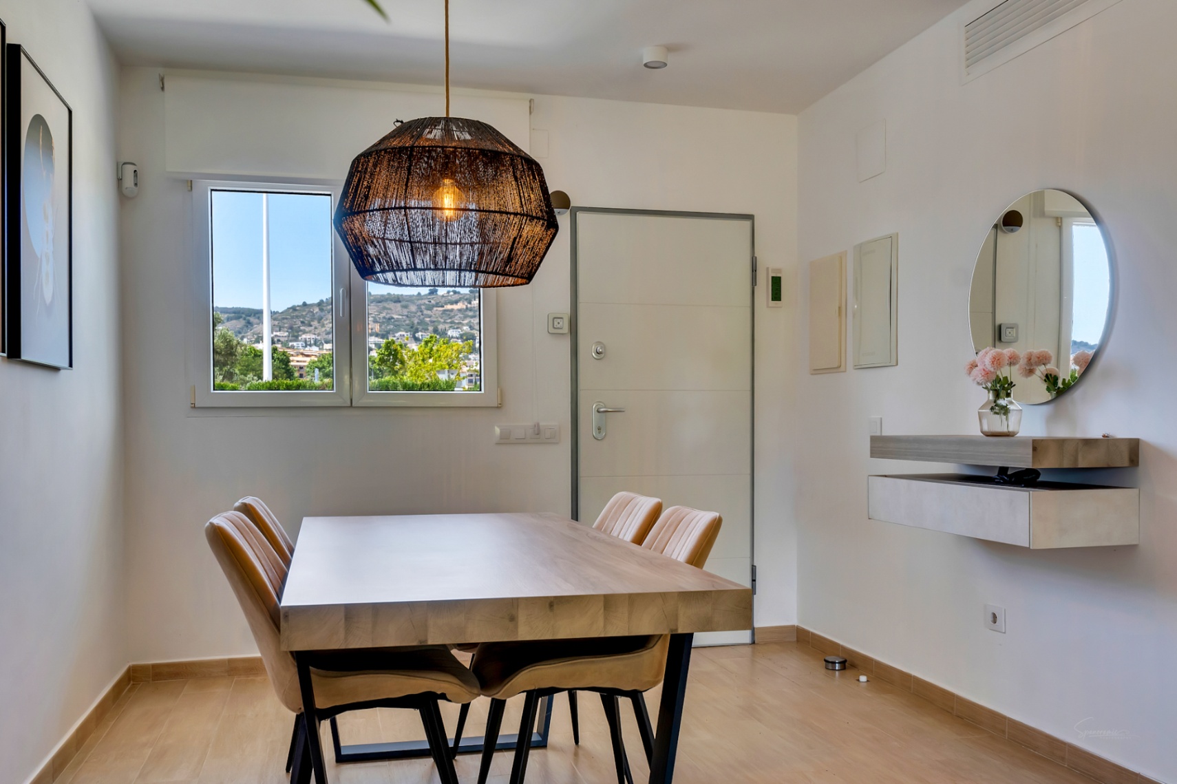 Espace salle à manger lumineux avec table en bois massif, suspension en fibres naturelles et vue dégagée. Console flottante moderne et miroir rond.