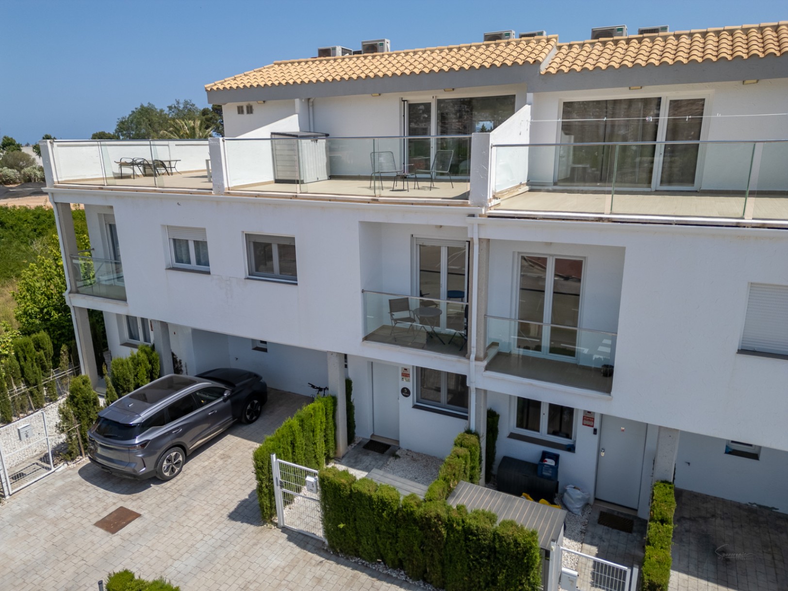 Façade moderne sur trois niveaux avec de grandes terrasses au dernier étage, garde-corps en verre et places de parking privées.