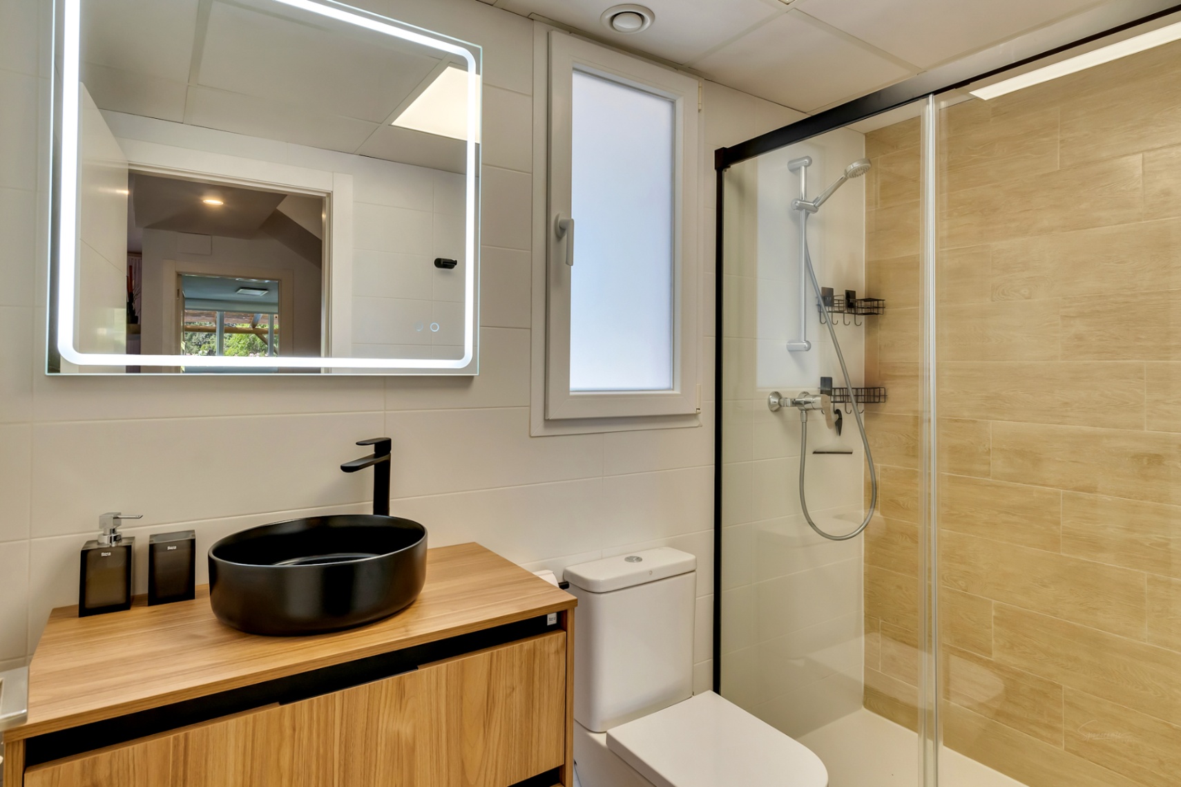 Salle de bain moderne avec vasque noire sur meuble en bois, miroir rétroéclairé et douche à l'italienne avec parois noires et carrelage aspect bois.