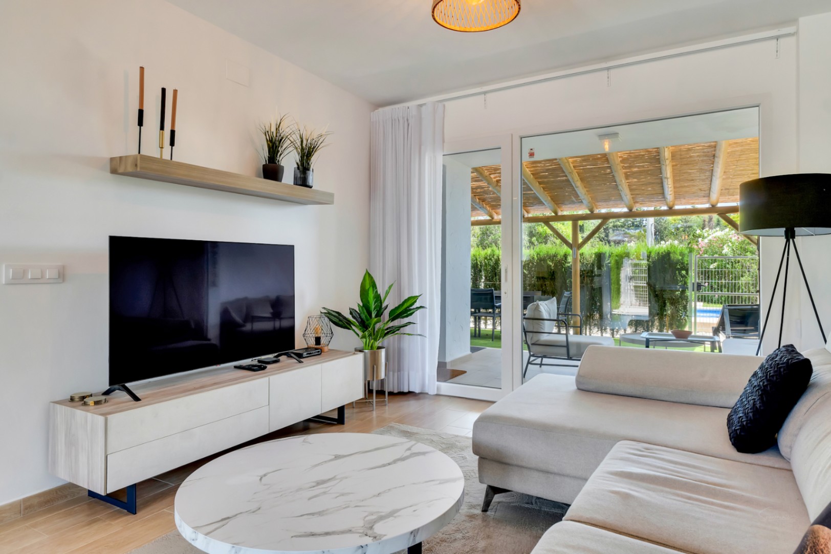 Salon à aire ouverte avec mobilier contemporain et grandes baies vitrées offrant un accès direct au patio privé abrité par une pergola en bois.
