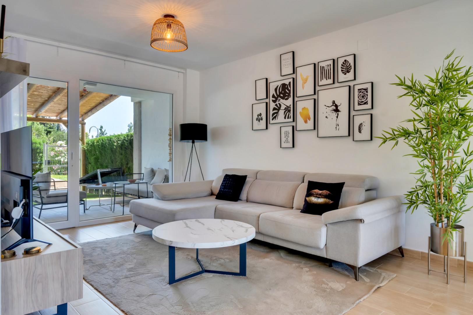 Salon lumineux avec canapé d'angle, table basse effet marbre et accès direct au patio privé par de grandes baies vitrées.