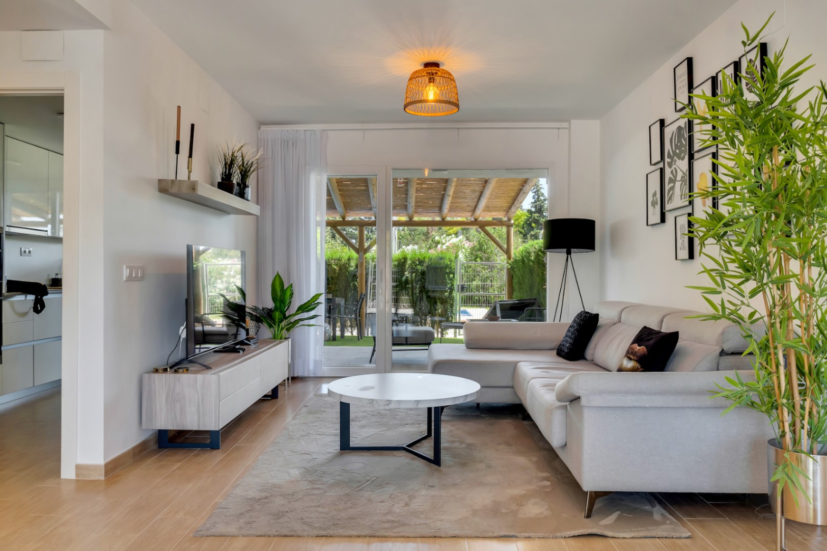 Salon lumineux avec carrelage imitation bois, mobilier moderne et grandes baies vitrées offrant un accès direct au patio privé et à la pergola en bois.