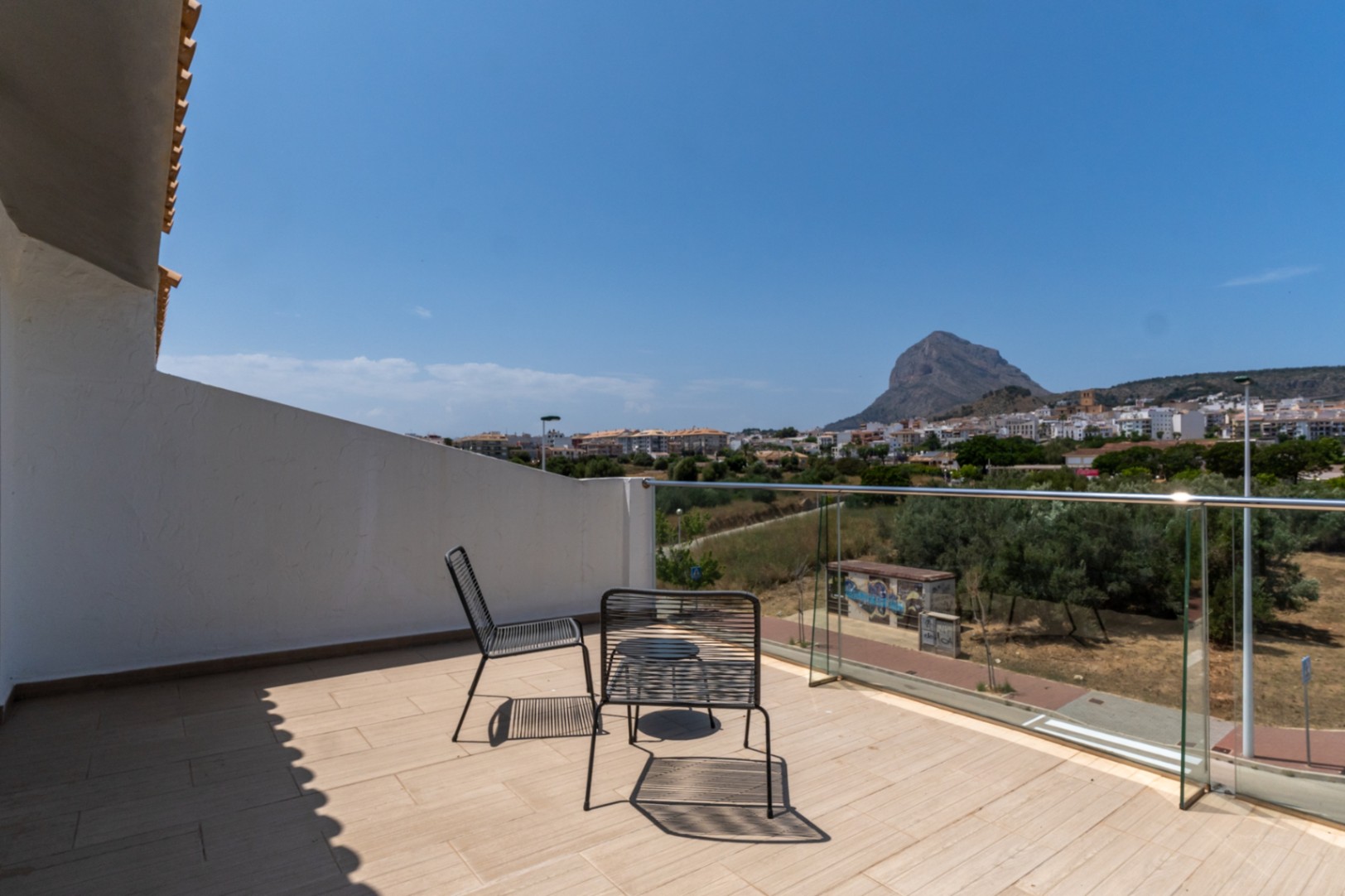 Terrasse à l'étage avec garde-corps en verre offrant une vue panoramique sur le Montgó et Jávea. Espace extérieur avec mobilier moderne et carrelage clair.