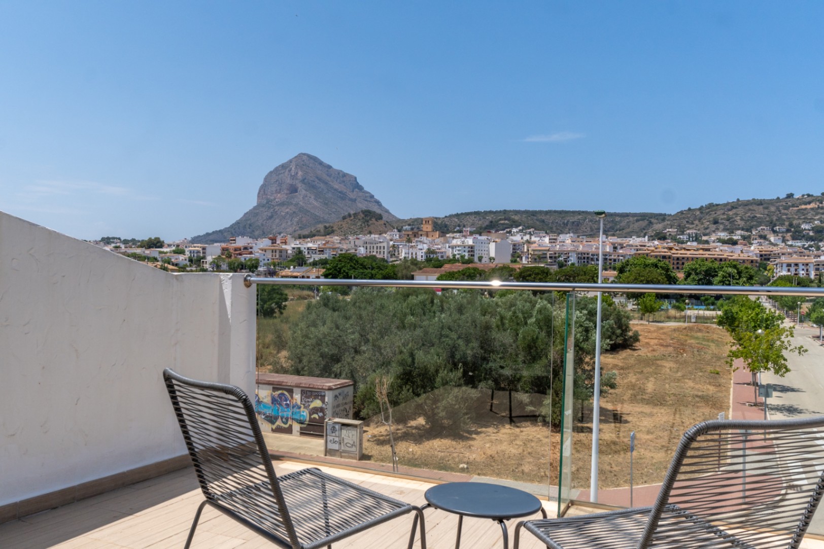 Terrasse privée au dernier étage offrant une vue panoramique sur le Montgó et la ville de Jávea, agrémentée d'un mobilier moderne et d'un garde-corps en verre.