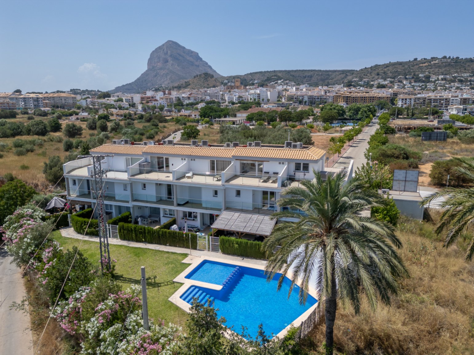 Vue aérienne du complexe résidentiel avec piscine commune et jardins, surplombé par le Montgó. L'architecture moderne se distingue par ses façades blanches et ses grandes terrasses.