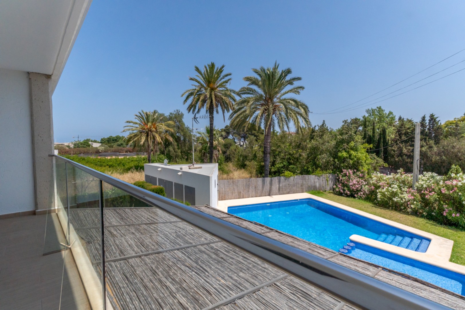 Vue depuis la terrasse supérieure avec garde-corps en verre, surplombant la piscine communautaire, les jardins méditerranéens et la pergola en bois du patio.
