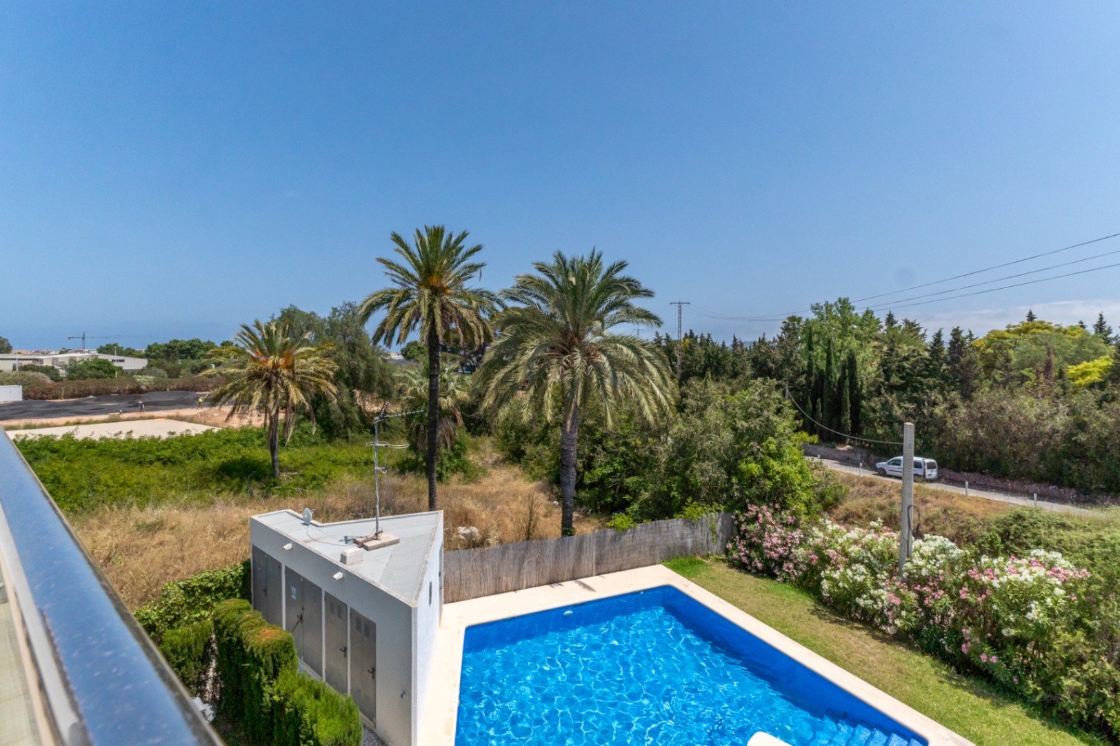 Vue depuis la terrasse supérieure sur la piscine communautaire, entourée de palmiers et de jardins soignés dans un environnement calme.
