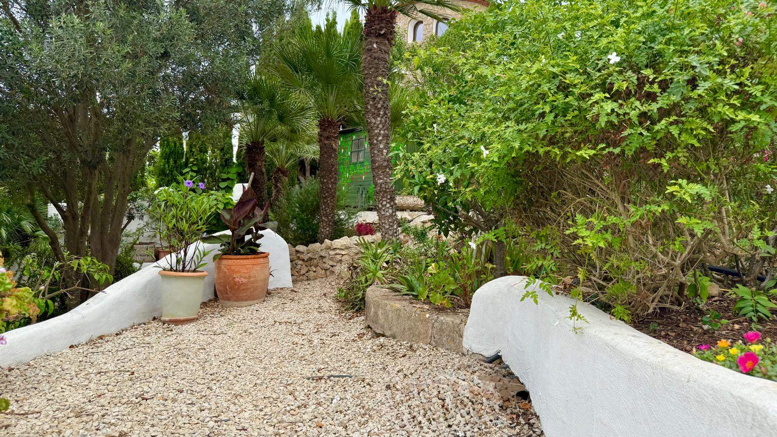 Allée de gravier dans le jardin méditerranéen, bordée de murets blanchis à la chaux, de pots en terre cuite et d'une végétation luxuriante.