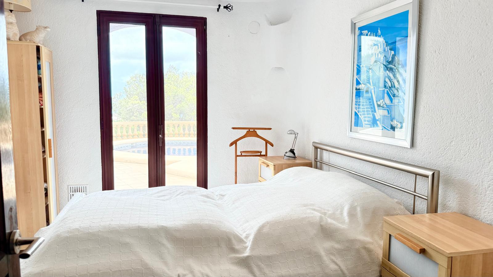 Chambre avec accès direct à la terrasse de la piscine, murs blancs texturés, mobilier en bois et vue sur l'extérieur par des portes vitrées.