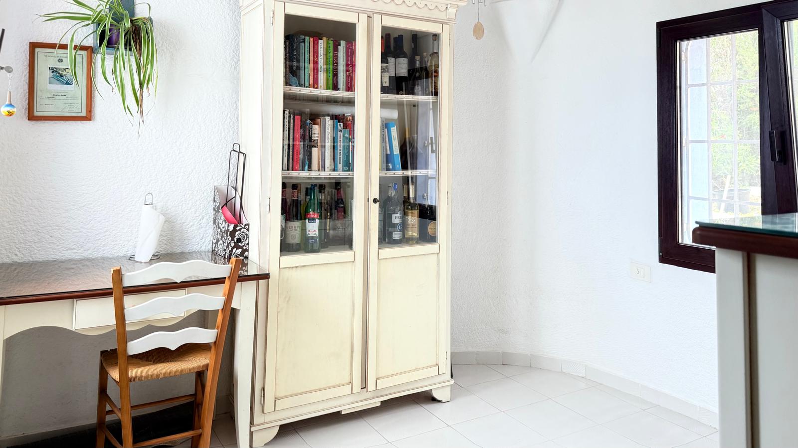 Coin bureau comprenant un secrétaire classique, une chaise en bois et une vitrine blanche de style traditionnel sur un sol en carrelage clair.