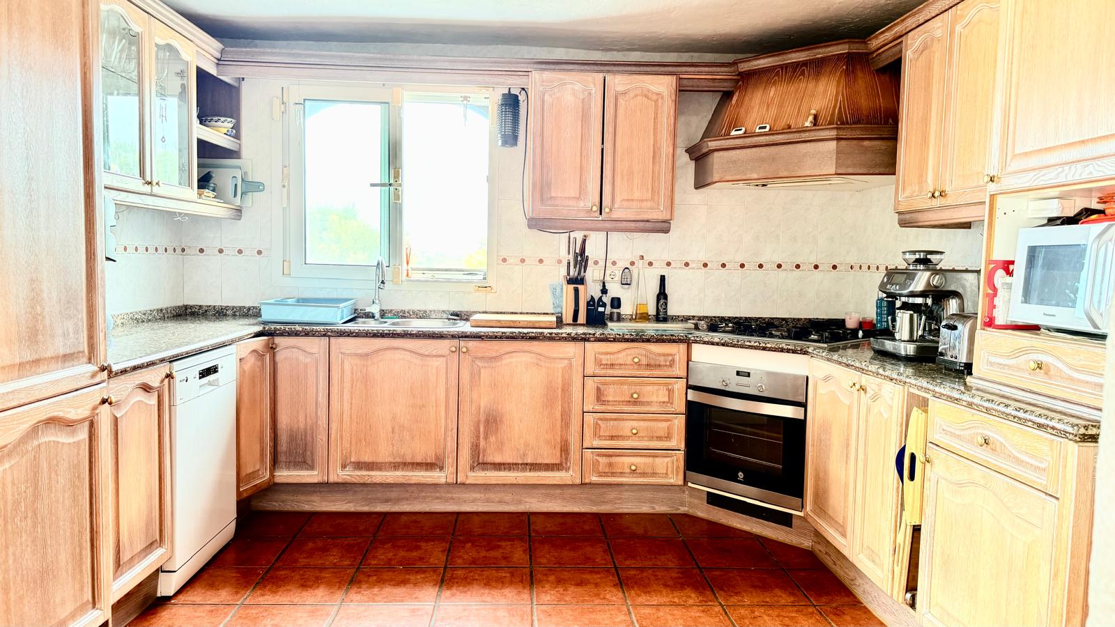 Cuisine de style traditionnel avec meubles en chêne, plans de travail en granit, sol en terre cuite et une fenêtre offrant une lumière naturelle sur l'évier.