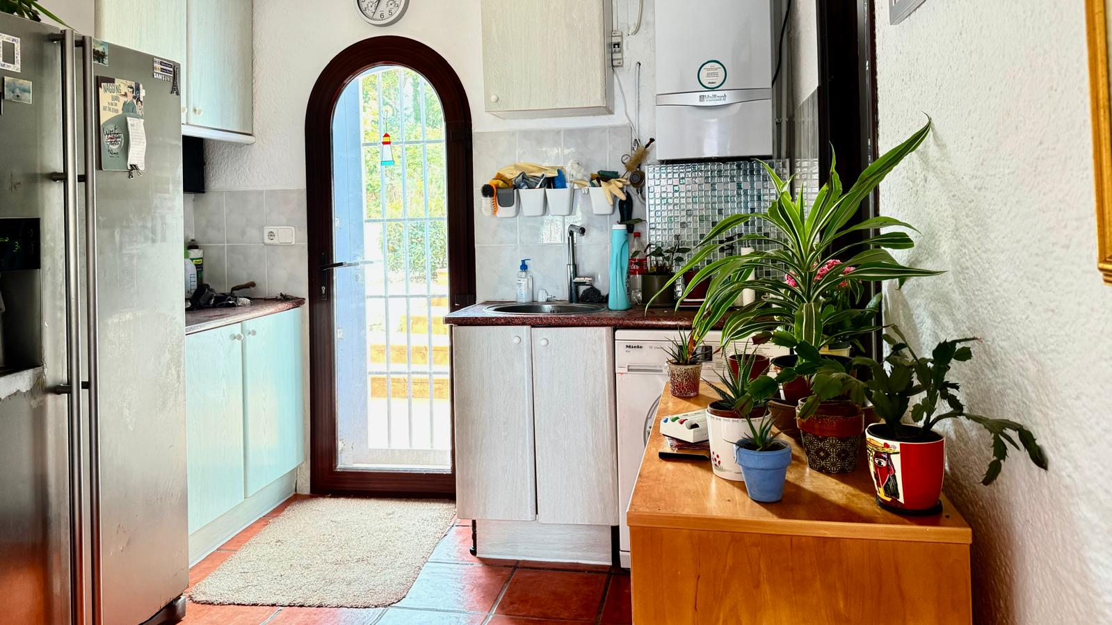 Cuisine fonctionnelle avec porte vitrée en plein cintre, plans de travail en granit et sol en terre cuite. Comprend des meubles blancs et un espace buanderie.