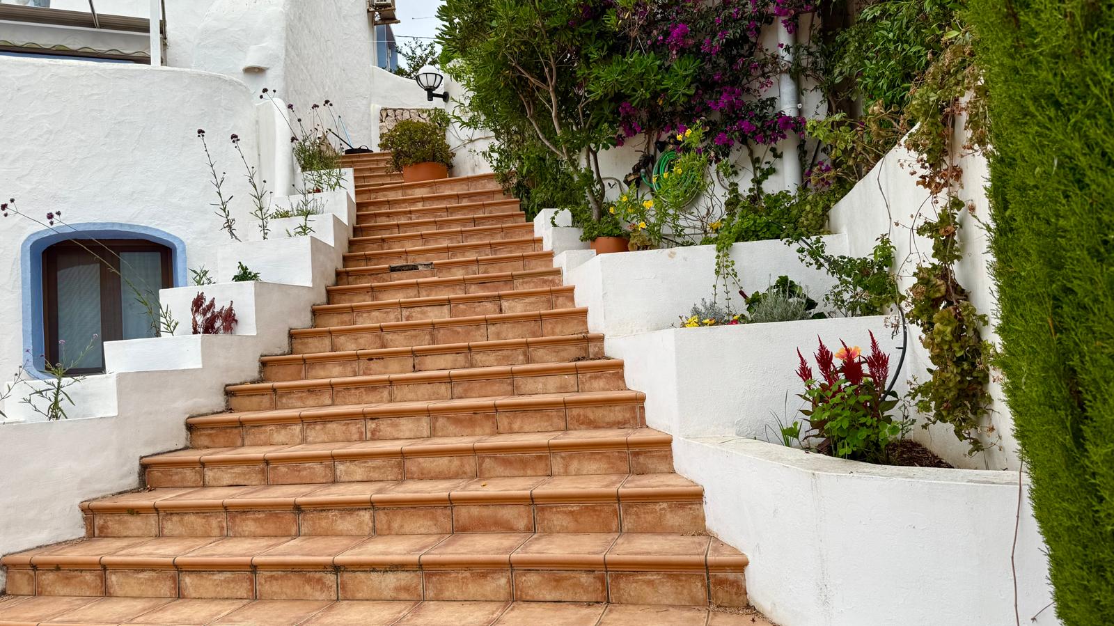 Escalier extérieur en terre cuite reliant les niveaux de la villa, bordé de jardinières blanches intégrées avec une végétation méditerranéenne et des bougainvilliers.